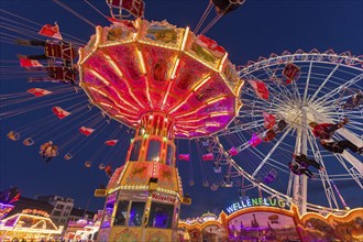 A funfair at dusk with illuminated chain carousel and Ferris wheel, Europa Rad, rides, wave flight,