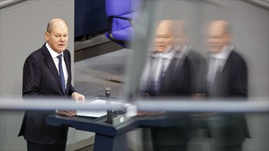 Federal Chancellor Olaf Scholz reflected in a pane of glass during his government statement in the