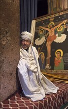 Ethiopian Orthodox priest in front of an image of the crucifixion of Jesus in the rock church of