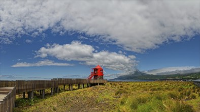 Wooden path leads to the Moinho das Lajes windmill with a dramatic sky and the volcanic cone of