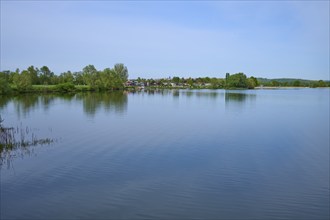 Quiet lake with trees on the shore, in the background a campsite, leisure area, under blue sky,