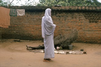 A hindu widow is giving alms to a leper (Puri, India) . The man is lying on the ground under a pile