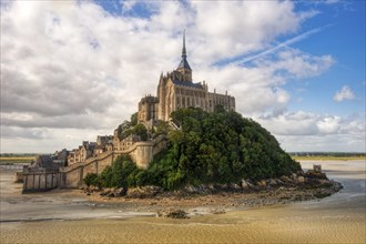 Abbey on a green hill in a vast landscape, surrounded by water and sand, Le Mont-Saint-Michel