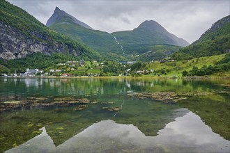 Mountainous landscape with a calm fjord reflecting the surrounding mountains and village,