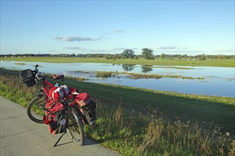 A bicycle stands at the edge of a dyke path next to a flooded Elbe meadow in a wide meadow