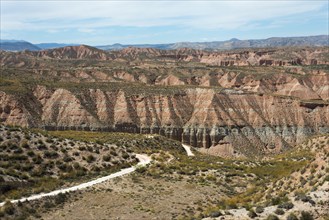 Wide hilly desert landscape with dry vegetation and gentle slopes under a slightly cloudy sky, Los