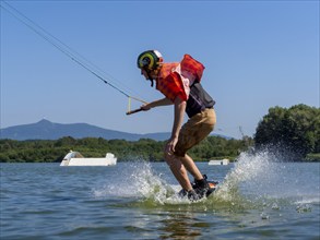 Young casual man with flapping shirt on wakeboard jumping into the lake, water ski and wakepark,