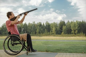 Senior man with paralysed legs in wheelchair aiming double-barreled shotgun at an outdoor shooting