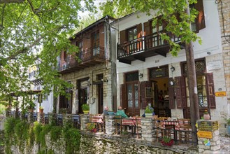 Cosy restaurant on a terrace overlooking green trees and traditional houses, Makrinitsa, Balcony of