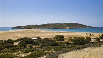 A quiet beach with sand dunes and a lush green island in the background under a bright blue sky,