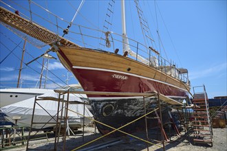 A large wooden sailing ship in dry dock with red paint and blue sky in the background, Patmos