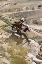 Traditional Kyrgyz eagle hunter hunting in the mountains in a dry landscape, near Kysyl-Suu, Issyk