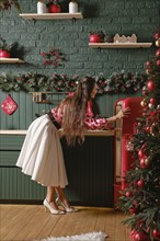 A woman opening a vintage red refrigerator amidst a beautifully decorated Christmas-themed kitchen.