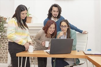 A group of young creative professionals working together at a desk in a bright office, looking at