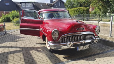 A shiny red vintage car with chrome details parked on a street on a sunny day, classic car, Buick