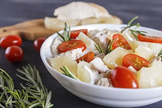 Chicken fillet salad with rosemary, pineapple and cherry tomatoes on dark blue wooden background.