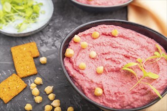 Hummus with beet and microgreen basil sprouts in ceramic bowl on a black concrete background and