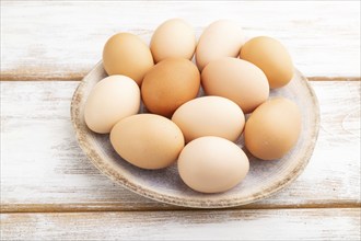 Pile of colored chicken eggs on plate on a white wooden background. side view, close up