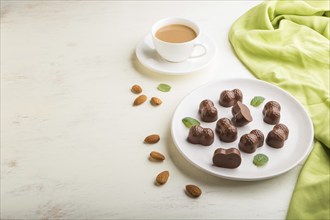 Chocolate candies with almonds and a cup of coffee on a white wooden background and green textile.