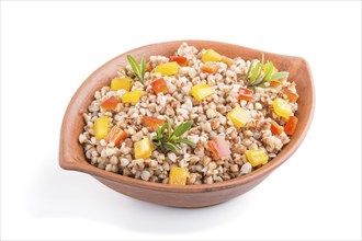 Buckwheat porridge with vegetables in clay bowl isolated on white background. Side view, close up.