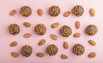 Chocolate caramel ball candies with almonds in a row on a pastel pink background. top view, flat