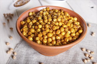 Fried chickpeas with spices in a clay plate on white wooden background, close up