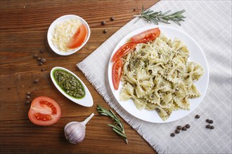 Farfalle pasta with pesto sauce, tomatoes and cheese on a linen tablecloth on brown wooden