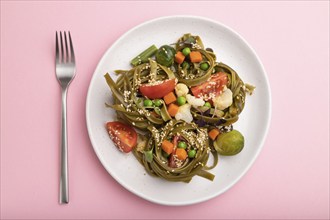 Tagliatelle green spinach pasta with tomato, pea and microgreen sprouts on a pastel pink background