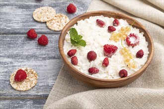 Rice flakes porridge with milk and strawberry in wooden bowl on gray wooden background and linen