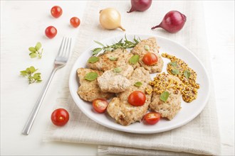 Fried pork chops with tomatoes and herbs on a white ceramic plate on a white wooden background and