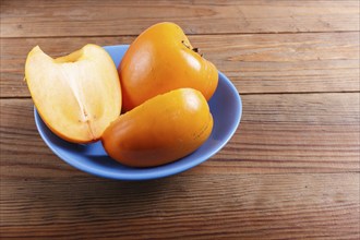 Ripe orange persimmon in a blue plate, on brown wooden background, with copy space