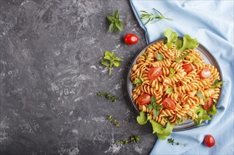 Fusilli pasta with tomato sauce, cherry tomatoes, lettuce and herbs on a black concrete background