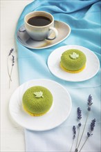 Green mousse cake with pistachio cream and a cup of coffee on a white wooden background and blue