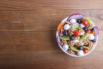 Salad with fresh cherry tomatoes, mozzarella cheese, olives, kiwi, onion and walnuts on brown