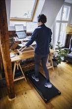 A woman walks on a walking pad at her desk while working from home. Berlin, 07.02.2024