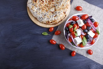 Greek salad with fresh cherry tomatoes, feta cheese, black olives, basil and onion on black wooden