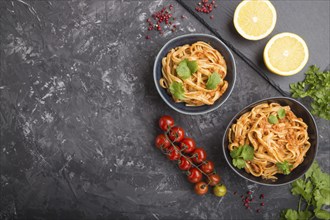 Semolina pasta with tomato pesto sauce, orange and herbs in bowls on a black concrete background.