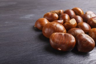 Pile of sweet chestnuts on black wooden background with copy space, top view