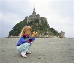 Little girl, age 7, examines what she found on the seabed in front of Mont Saint Michel, Normandy,