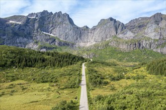 Aerial view of road in mountain scenery, passing lakes and meadows, road from E10 to village