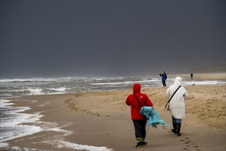 Walkers on the beach, dark storm clouds, choppy sea, autumn on the North Sea in North Holland,