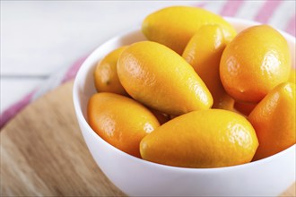 Kumquats in a white plate on a white wooden background, close up