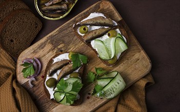 Sandwiches, black bread with sprats, cream cheese, cucumbers, on a cutting board, top view,