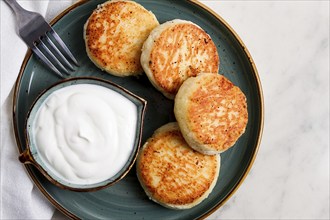 Fried, Cottage cheese pancakes, with sour cream, Cheesecakes, on a marble table, top view, no