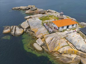 A lighthouse on a rocky island, surrounded by clear water, with an orange-coloured roof and a small