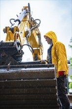 Construction worker in yellow rain jacket working with large construction machine in the rain,