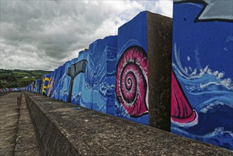 Colourful mural by the sea with a large pink snail under a cloudy sky, small town of Vila Franca do