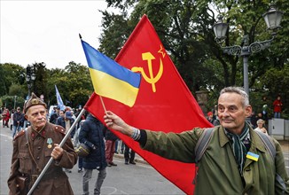 A Ukrainian man holds a Ukrainian flag in front of the former flag of the Soviet Union held by a