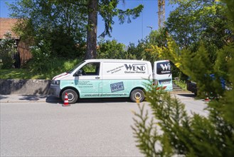 A company delivery van with company logo parked on the roadside under a blue sky next to trees and