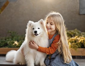 A girl with long hair holds a white dog in her arms on a wooden terrace in the golden sunlight, dog